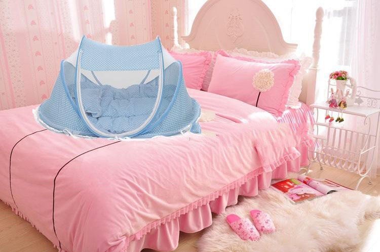 Foldable baby bed net in blue, set on a pink bed with cozy pillows, providing safe sleep space for infants