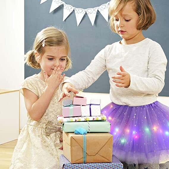 Two kids excited by gifts, one wearing a magical LED tutu skirt for kids in purple with glowing lights.