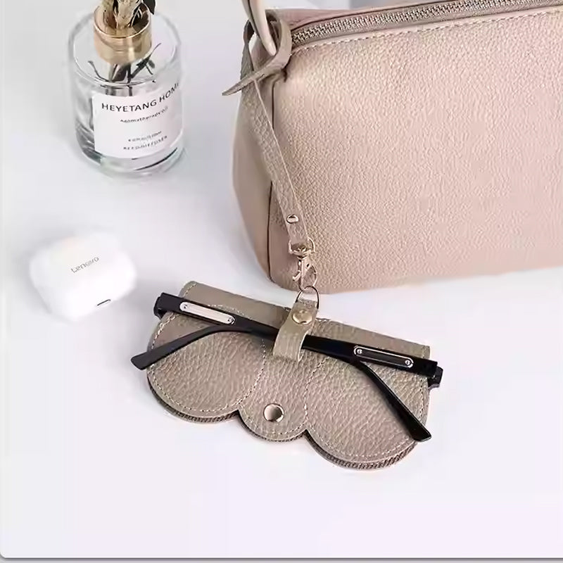 Stylish fashion sunglasses case in light beige leather, featuring a clip and elegantly storing black sunglasses.